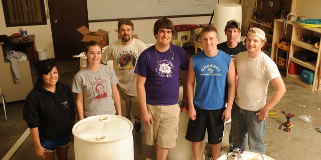 The Hesston College Entrepreneurship class takes a break from turning 55-gallon food-grade drums into rain barrels. 