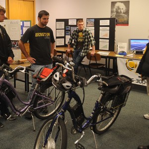 Hesston College physics students Keenan Jensen and Ron Wenger talk with Earth Day guests about the electric bicycles with solar power charging stations they helped build.