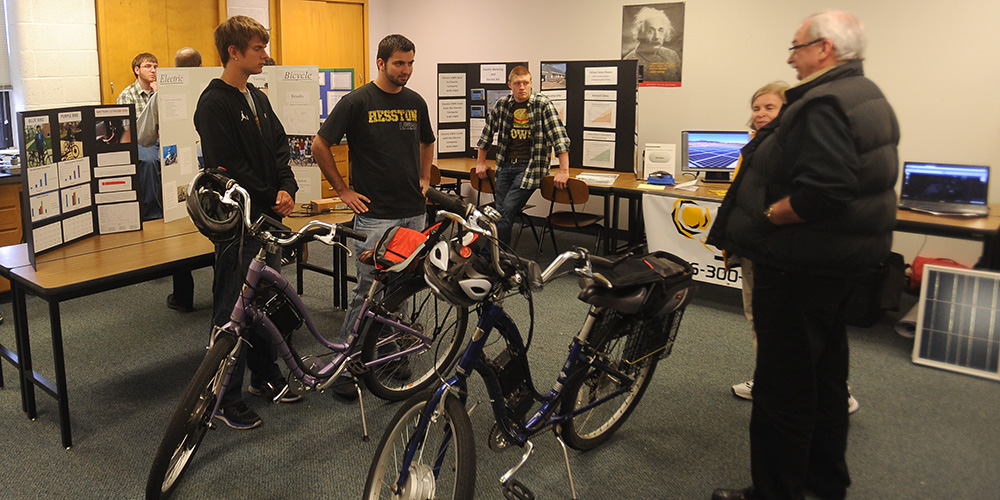 Hesston College physics students Keenan Jensen and Ron Wenger talk with Earth Day guests about the electric bicycles with solar power charging stations they helped build.