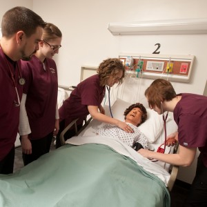 Hesston College Nursing students Chad Jones (Halstead, Kan.), Jennifer Kaberline (McPherson, Kan.), Brianne Stutzman (Hesston, Kan.) and Rinda Amstutz (Goessel, Kan.) practice on a sim patient in an on-campus nursing lab.