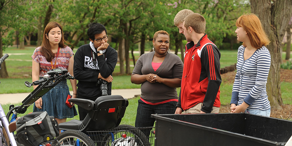 Natural science instructor Marelby Mosquera (third from left) talks with a group of students about the solar-charged personal activities vehicle built by students in the college’s Physics II course.