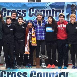 Hesston College's women's cross country team poses in front of a banner at the NJCAA national meet.