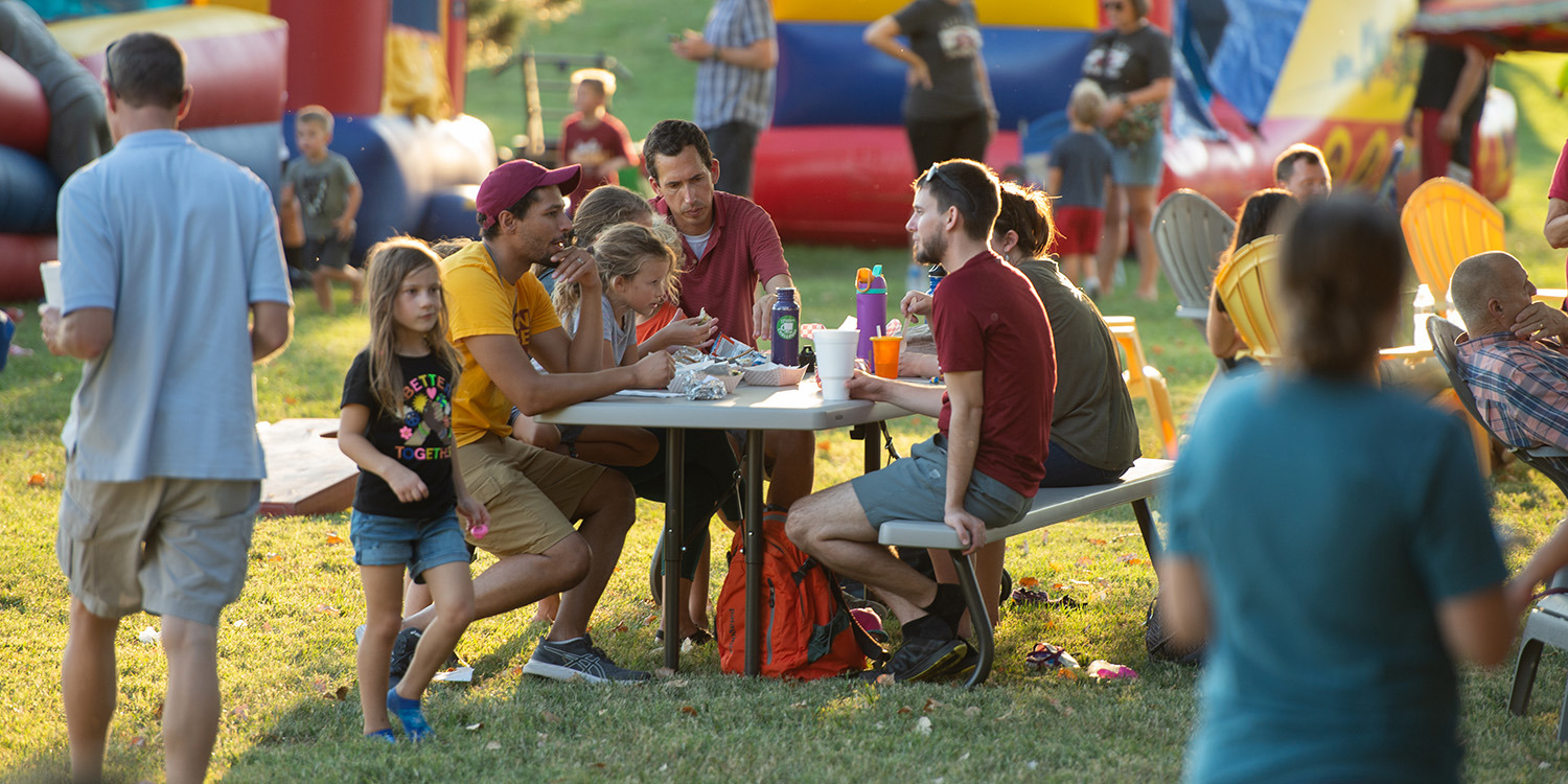 Fall 2022 community day - families eat at a picnic table with bouncy houses in the background