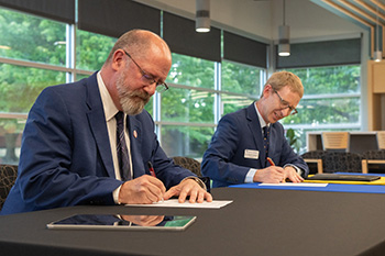 photo - Hesston College Interim President Ross Peterson-Veatch, Ph.D., and Tabor College President David Janzen, Ph.D., sign the memorandum of understanding allowing both colleges to offer courses and degrees to students at their respective institutions.